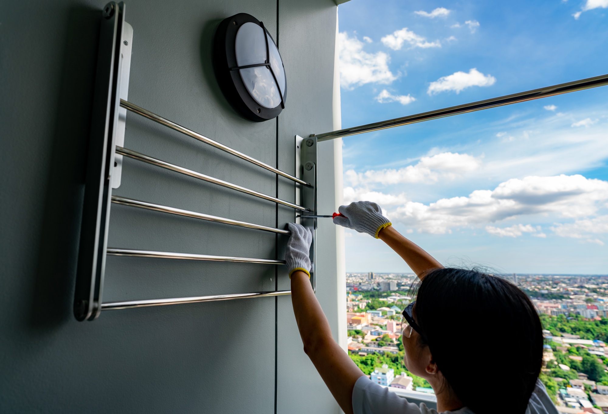 Asian woman use screwdriver screwing screw into the apartment wall for install clothes line. Thai