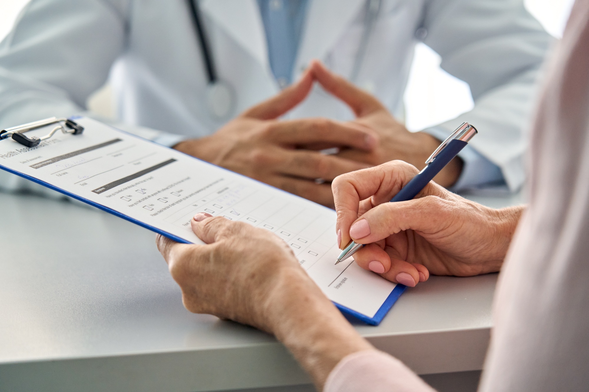 Closeup older patient filling medical heath data form in hospital clinic.