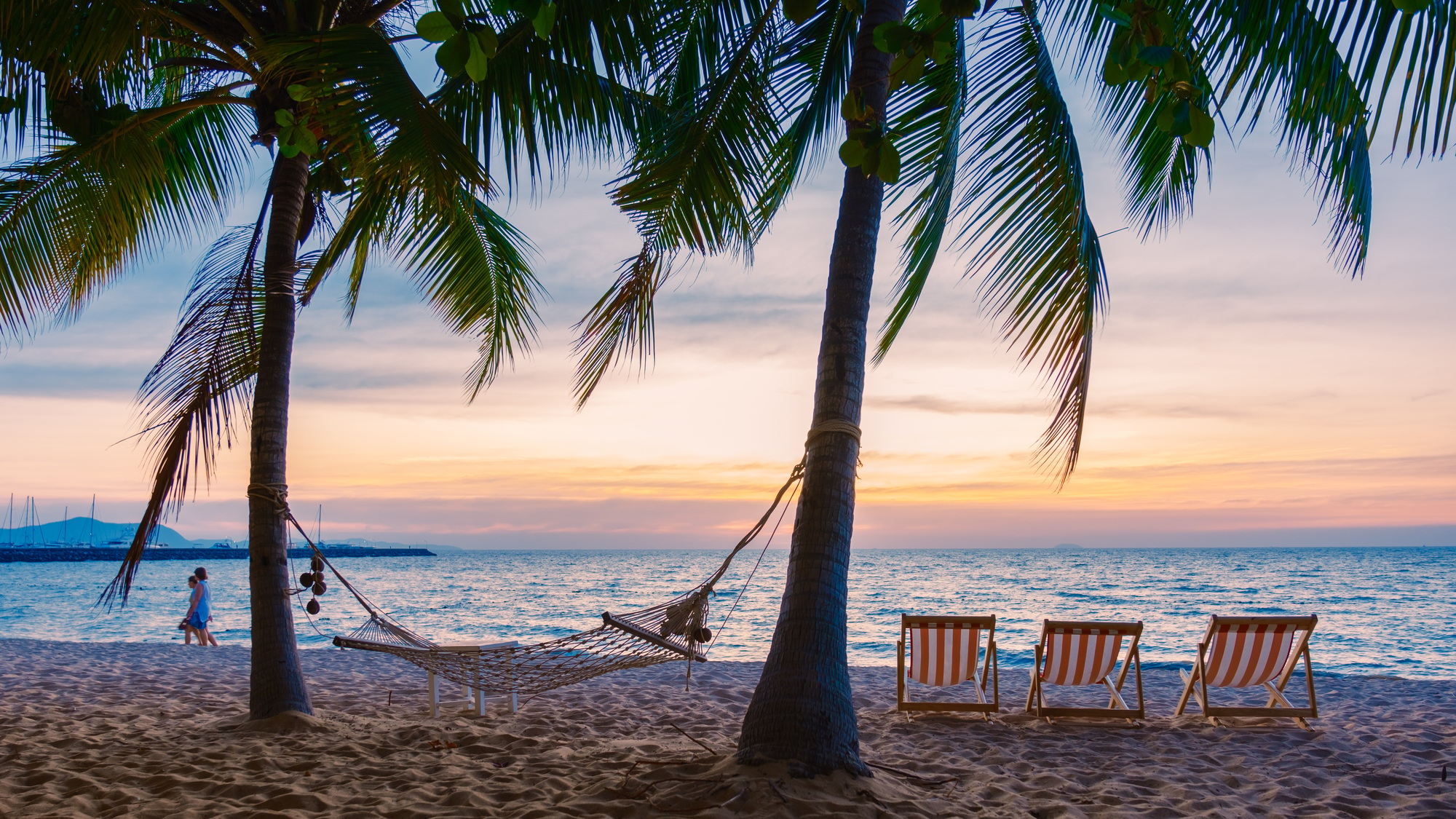 Hammock and beach chairs on the beach with palm trees during sunset at Na Jomtien Beach Pattaya