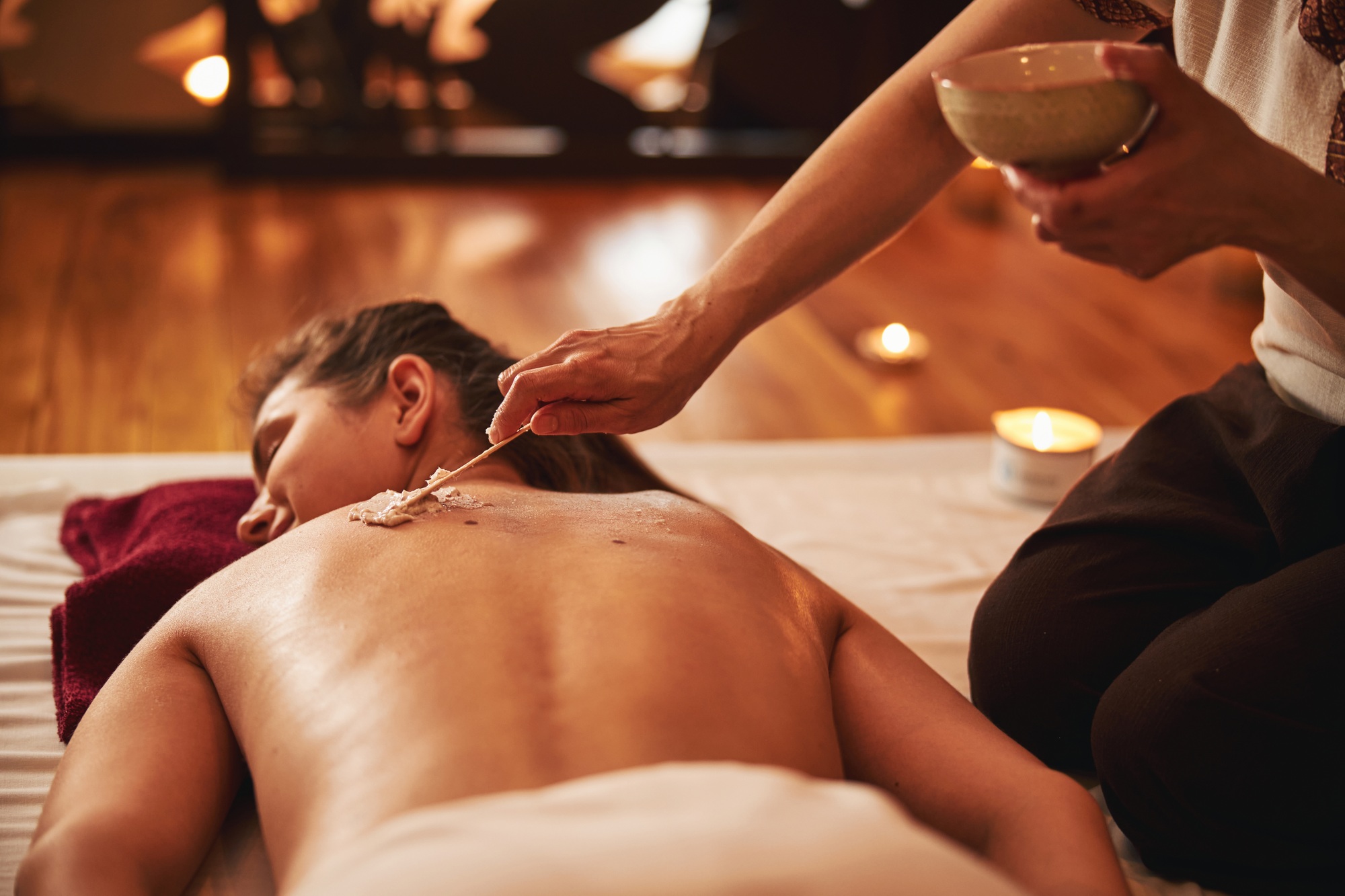 Massage worker evenly applying cream on back with wooden stick