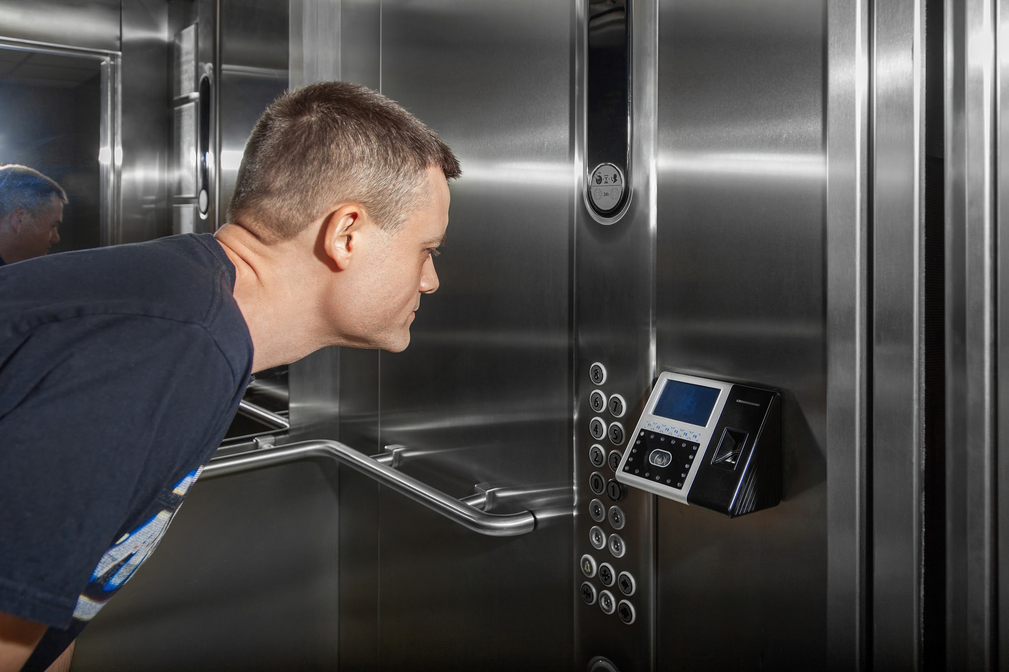 Man shows face to fingerprint access control terminal with facial recognition function in elevator