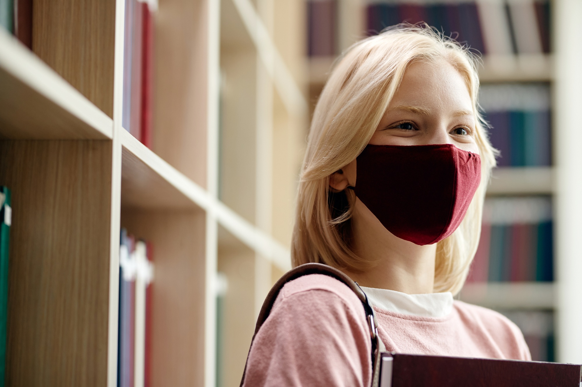 Happy college student wearing face mask in a library during coronavirus pandemic.